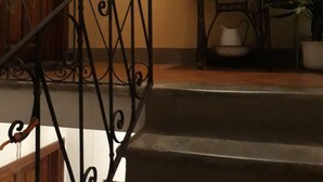 Un escalier avec une rampe en fer forgé, une porte en bois, un tableau encadré au mur, une petite table avec une lampe et une plante en pot.
