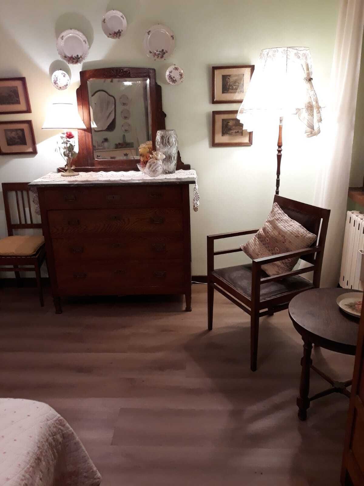 A room with a wooden dresser, a chair, a small table, and a lamp.