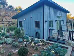 Standalone desert dwelling with a small porch and cacti surroundings.