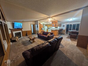 Una sala de estar con chimenea, un sofá, televisión y una cocina al fondo.