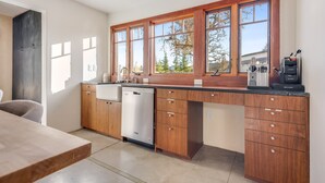 A modern kitchen with wooden cabinets, a dishwasher, and a large window providing a view of trees. - Harmony Over The Hill (Templeton)