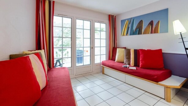 Une pièce avec un canapé rouge, un banc et un mur orné d’un tableau représentant des planches de surf.