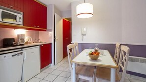 Une cuisine de taille réduite avec des placards rouges, un four à micro-ondes, un évier et une table à manger avec des chaises.