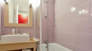 Une salle de bain avec une baignoire blanche, un meuble-lavabo en bois avec un miroir et des murs recouverts de carreaux roses.