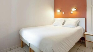 Une chambre avec un lit simple, un lit blanc, deux lampes fixées au mur et un mur de couleur orange unie.