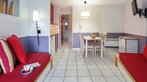 Un espace de vie compact comprenant un coin cuisine, un coin repas et un canapé avec des coussins rouges.