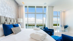 Una habitación de hotel moderna con una cama grande, almohadas azules y blancas, un escritorio y vistas al exterior.