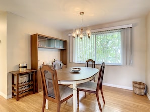 A dining area with a round table, four chairs, a chandelier, a window with blinds, and a wooden cabinet with shelves. - Cozy Whole Home Half Mile From Venice Island (Venice)