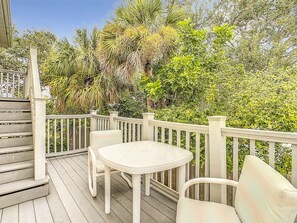 A wooden deck with a white table and chairs, surrounded by lush greenery and trees.