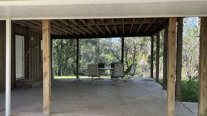 A covered outdoor patio with a concrete floor, wooden pillars, and a table with four chairs. - Mark and Bobby’s Island (Wharton)