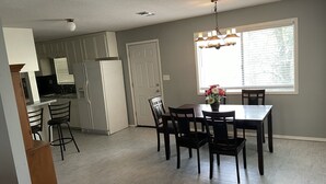 A modern kitchen with white cabinets, a refrigerator, and a dining area with a table and chairs. - Mark and Bobby’s Island (Wharton)
