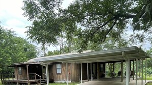 A rustic cabin with a covered porch and a small deck area. - Mark and Bobby’s Island (Wharton)