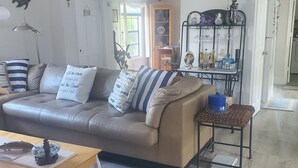 A living room with a brown leather sofa, a coffee table, and a side table with a basket. There is a ceiling fan and a decorative item hanging from the ceiling. - Key Largo heavenly retreat (Key Largo)