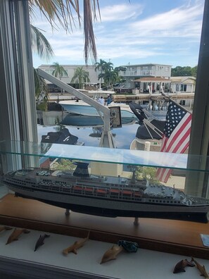 A model ship on a display shelf with a view of a marina and buildings in the background.
