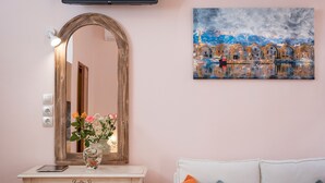 A room with a white sofa, a wooden console table with a vase of flowers, a mirror, and a painting of a coastal scene. - Luxury king size studio with terrace at the heart of Chania old town (Chania)