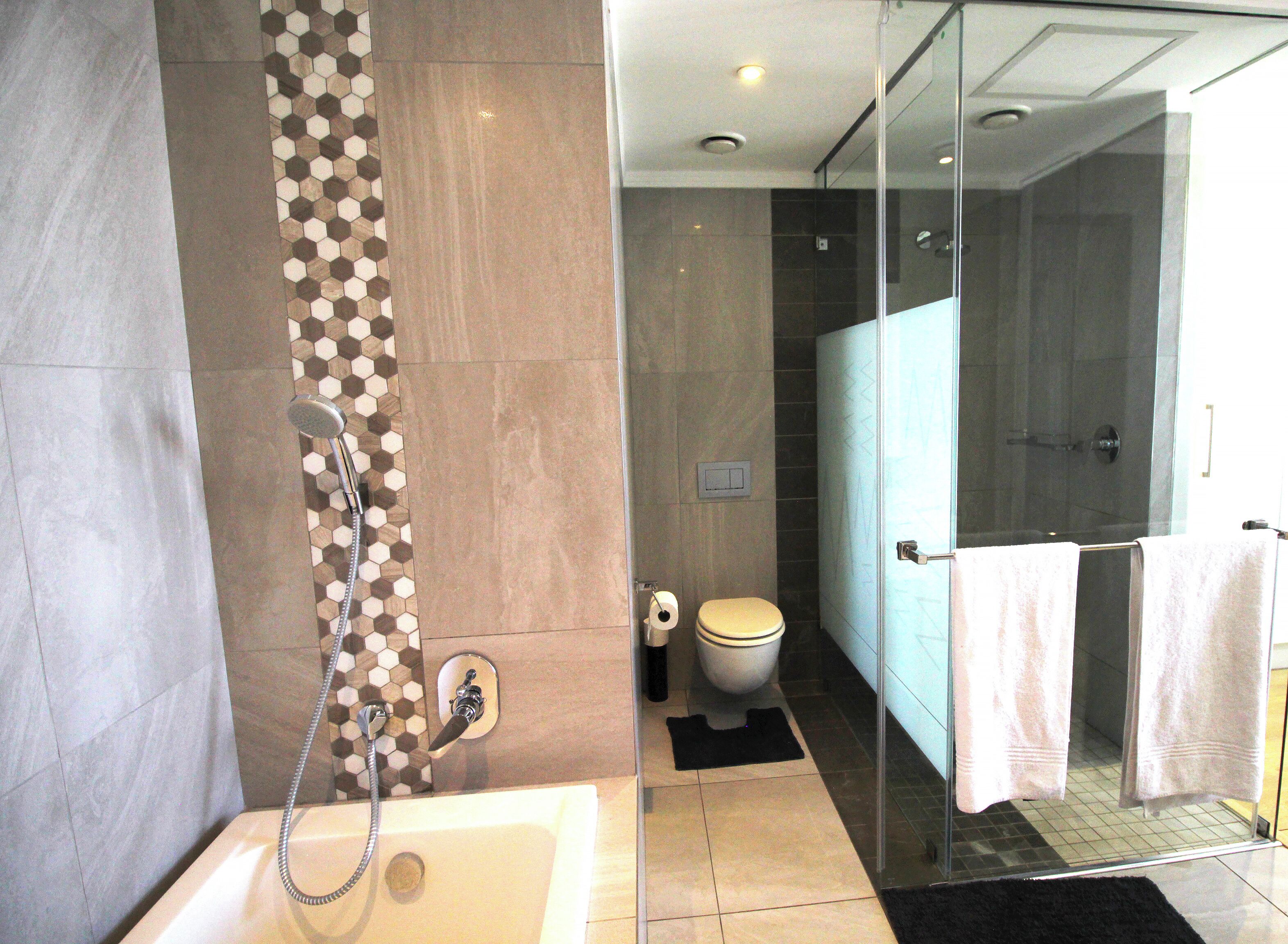 A modern bathroom with a glass shower enclosure, a bathtub, and a toilet.