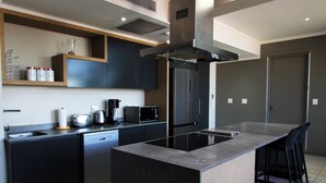 A modern kitchen with a central island, dark cabinetry, and a built-in microwave. - Sandton Smart Apartment Sixteen (Sandton)