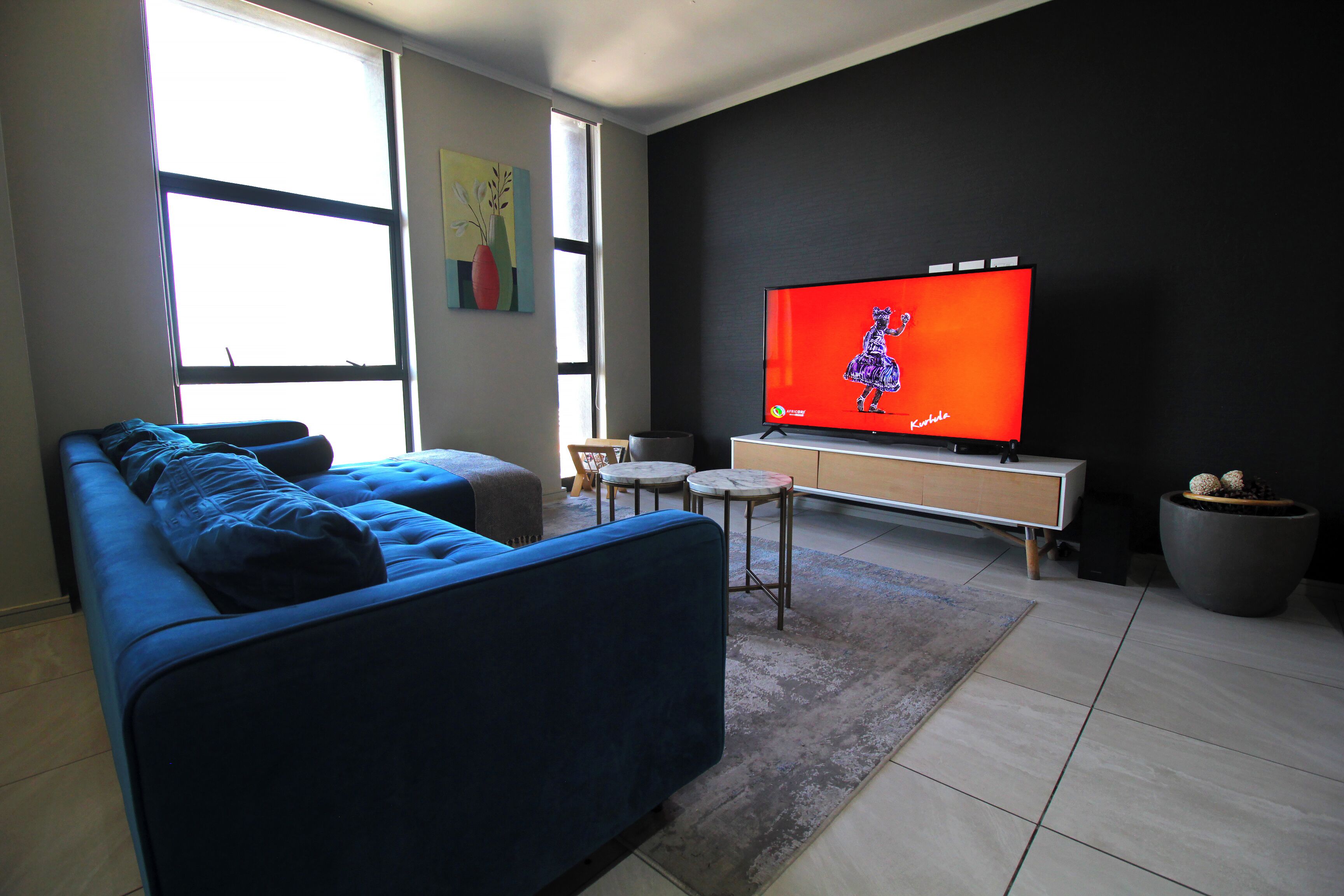 Una sala de estar moderna con un sofá azul, un televisor de pantalla plana, una pequeña mesa de centro y una planta en maceta.
