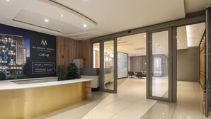 A modern reception area with a reception desk, a large poster advertising Masingta Towers, and a glass door leading to a well-lit interior space. - Sandton Smart Apartment Sixteen (Sandton)
