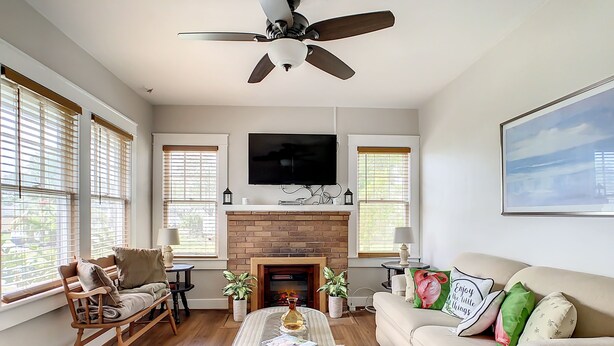 Un salon avec une cheminée, un ventilateur de plafond, un téléviseur et un canapé.