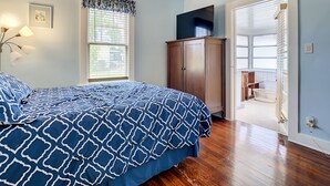 Une chambre à coucher comprenant un lit, une armoire, un téléviseur et une fenêtre avec des stores.