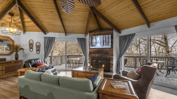 A cozy living room with a fireplace, a large sofa, and a dining area with outdoor seating. - Slopeside Beech Mtn - Ski-In/Ski-Out - Beat the Heat - Biking + Mountain Views (Beech Mountain)
