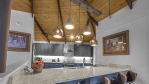 A modern kitchen with a large island, bar stools, pendant lighting, and dark cabinetry. - Slopeside Beech Mtn - Ski-In/Ski-Out - Beat the Heat - Biking + Mountain Views (Beech Mountain)