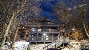 A multi-story building with a balcony and stairs, surrounded by trees and snow. - Slopeside Beech Mtn - Ski-In/Ski-Out - Beat the Heat - Biking + Mountain Views (Beech Mountain)