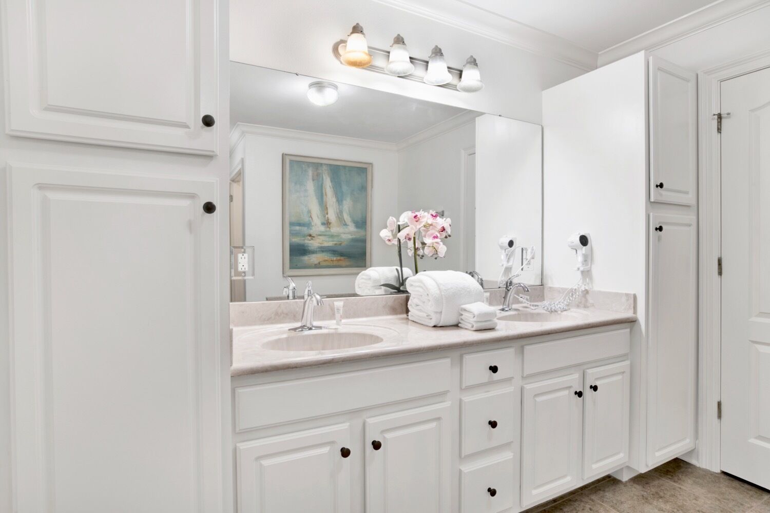A white bathroom with a double sink vanity, a large mirror, and a painting of sailboats.