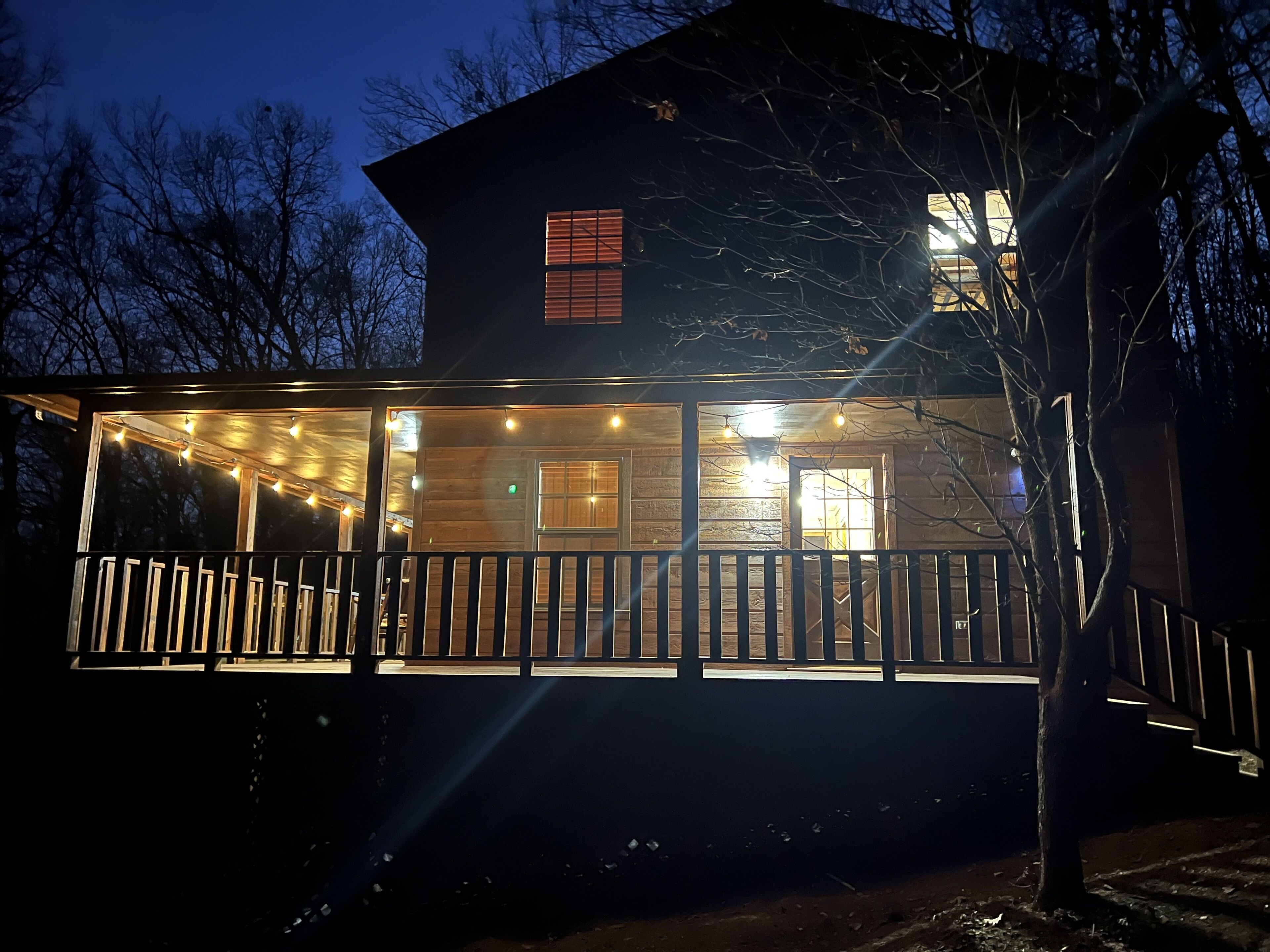 A wooden cabin with a porch, string lights, and a visible window.