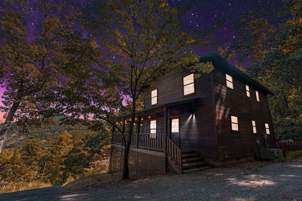 A wooden cabin with a balcony, surrounded by trees and a starry sky.