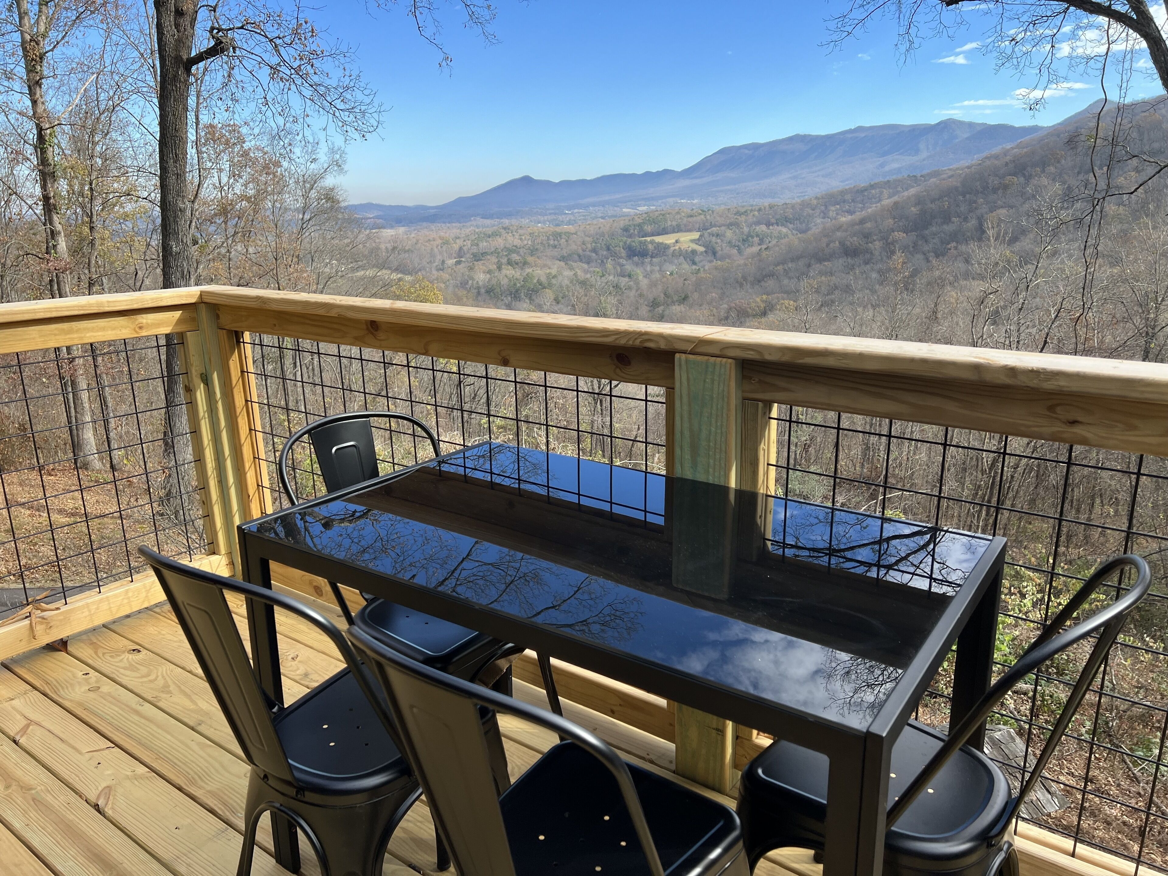 A wooden deck with a glass table and metal chairs overlooking a mountainous landscape.