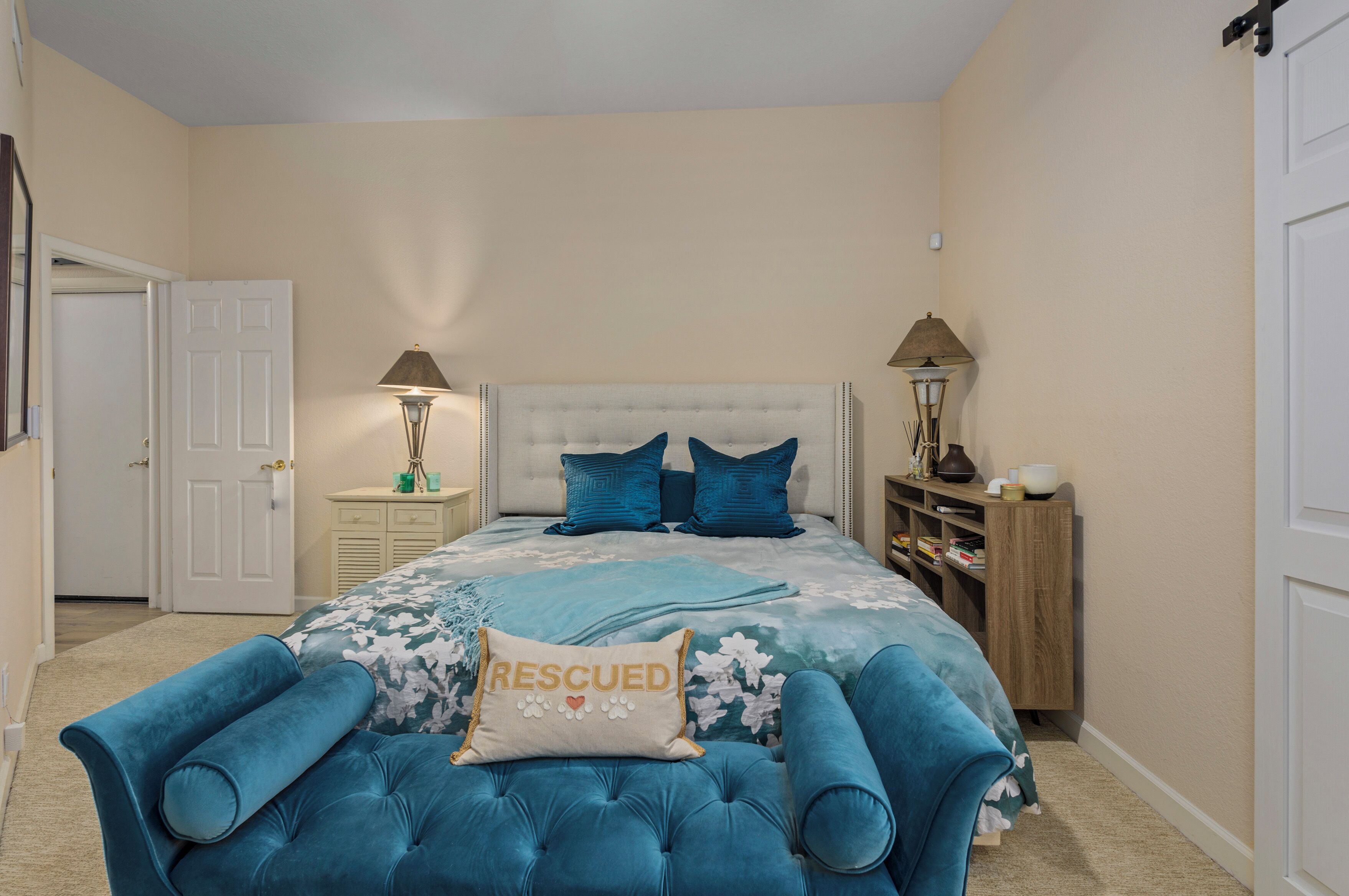 A bedroom with a tufted headboard, a floral bedspread, and a 'rescued' pillow.