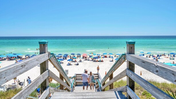 A wooden staircase leading to a beach with umbrellas and people.