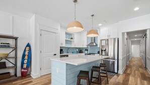 A modern kitchen with a central island, pendant lights, and a surfboard decoration.