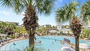 A resort pool area with palm trees, lounge chairs, and a clear blue sky.
