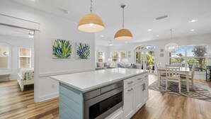 A modern kitchen with a central island, pendant lights, and a dining area with a view.