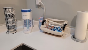 Eine Kaffeemaschine, eine Taschentuchbox und eine Toilettenpapierrolle auf einer weißen Arbeitsplatte.