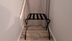 Ein kleines Zimmer mit einer Metallbank, einem weißen Handtuchhalter und einem grauen Vorhang.