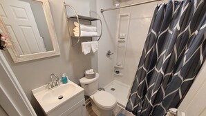 Ein Badezimmer mit einem weißen Waschbecken, einer Toilette und einem Duschvorhang. Über der Toilette befindet sich ein Handtuchhalter und auf dem Boden liegt ein blauer Teppich.