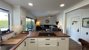 Een moderne keuken met witte kasten, een houten aanrecht en een zithoek met een bank en een lamp.