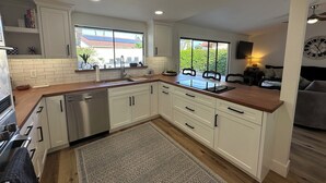 Een moderne keuken met witte kasten, een houten aanrechtblad en een ingebouwde vaatwasser. Een groot raam biedt uitzicht op de omgeving.