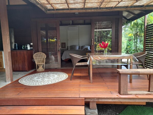 A wooden deck with a dining table and chairs, a sofa, and a small kitchen area with a coffee maker.