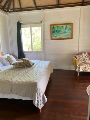 A room with a bed, a chair, a window, and a painting on the wall.