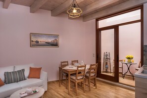 Un salon chaleureux avec un canapé blanc, une table à manger en bois entourée de chaises, un tableau accroché au mur et une porte-fenêtre coulissante donnant sur un balcon où se trouvent une baignoire et une petite table agrémentée de fleurs.