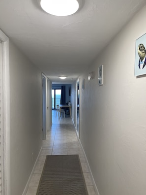 A hallway with a tiled floor, a vent, and a door leading to a room. - Beachfront piece of heaven! (Daytona Beach Shores)