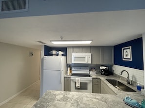 A compact kitchen with white appliances, a marble countertop, and blue walls. - Beachfront piece of heaven! (Daytona Beach Shores)