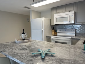 A kitchen with a marble countertop, a refrigerator, a microwave, and an oven. - Beachfront piece of heaven! (Daytona Beach Shores)