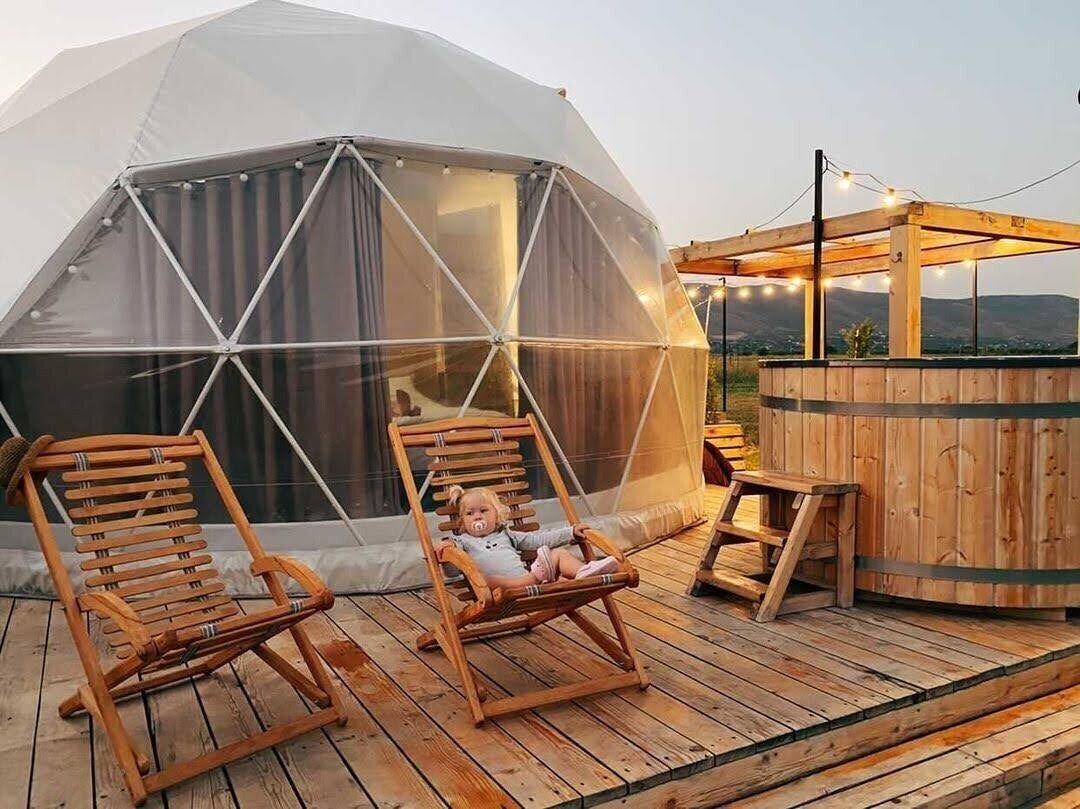 A geodesic dome structure with a wooden deck, two wooden lounge chairs, and a wooden bar area.