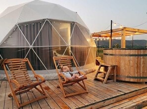 A geodesic dome structure with a wooden deck, two wooden lounge chairs, and a wooden bar area. - Jewelberry Glamping (Mtskheta)